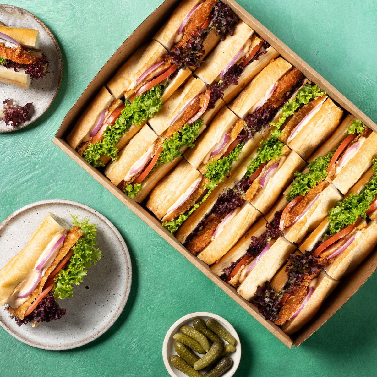 Box of sub sandwiches with greenery on a teal background